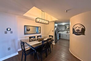 A dining area with a rectangular table, four chairs, a chandelier, and a wall-mounted mirror. - 6th floor condo- hot tub- views of Grandfather Mountain (Sugar Mountain)