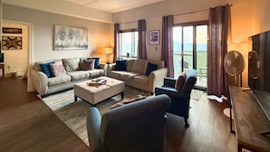 A modern living room with a sofa set, a coffee table, and a TV. There are two windows with curtains, and a balcony is visible through the windows. - 6th floor condo- hot tub- views of Grandfather Mountain (Sugar Mountain)