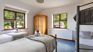 Ein Zimmer mit zwei Betten, einem Holzschrank, einem Heizkörper und einem Fenster mit Blick auf Bäume und ein Haus.