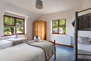 Ein Zimmer mit zwei Betten, einem Holzschrank, einem Heizkörper und einem Fenster mit Blick auf Bäume und ein Haus.