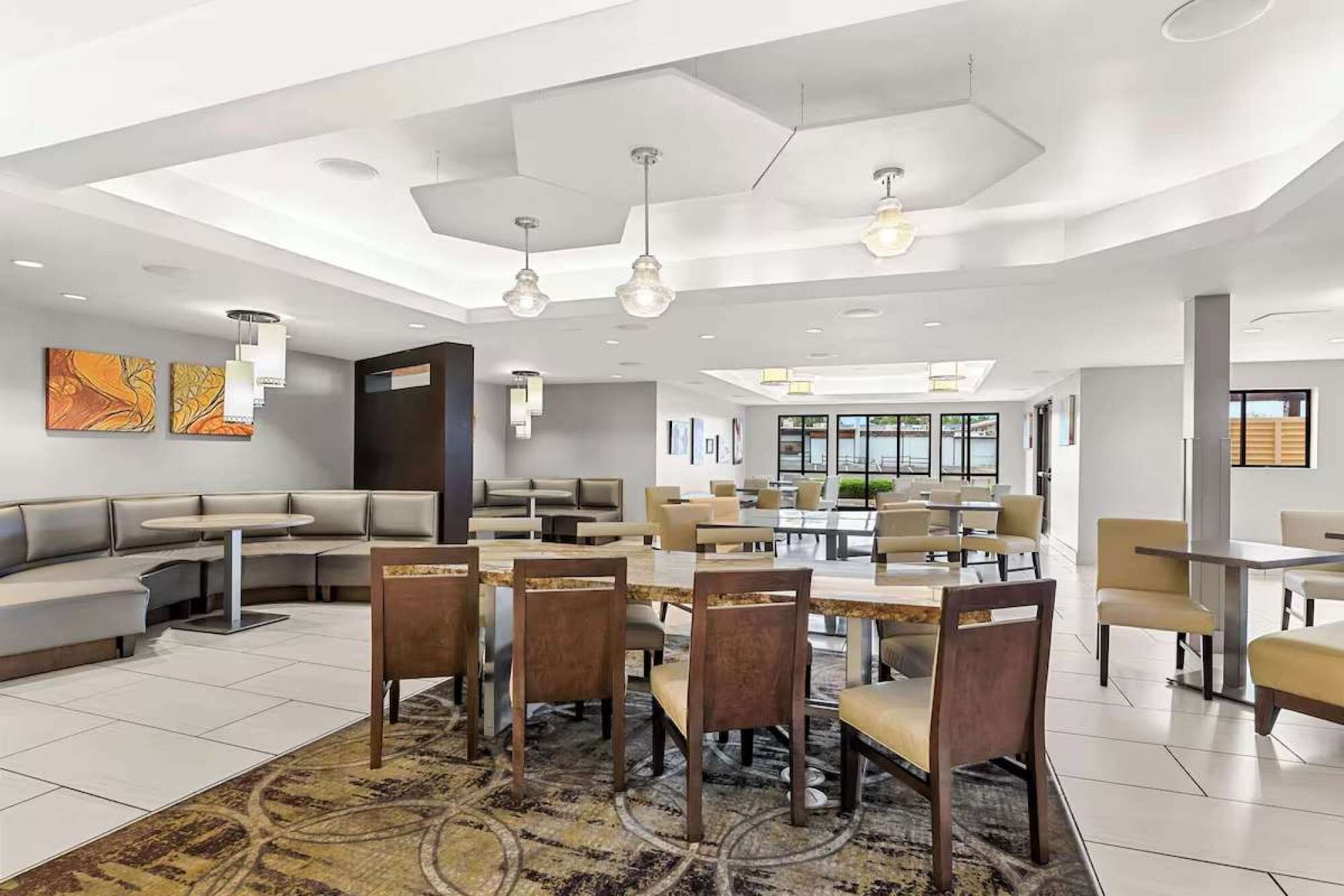 A modern dining area with multiple seating options, including round tables and booths, and a large window providing a view of the outdoors.