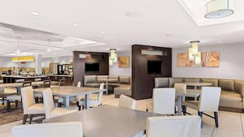 Een moderne hotellobby met zithoeken, een bar en een televisiescherm.