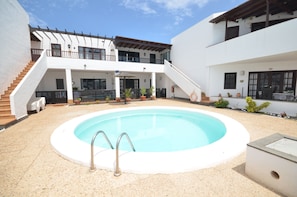 A swimming pool with a metal ladder, surrounded by a covered patio area with steps leading up to a balcony. - Serendipia Apartment Well Located, Pool & Terrace (Tías)