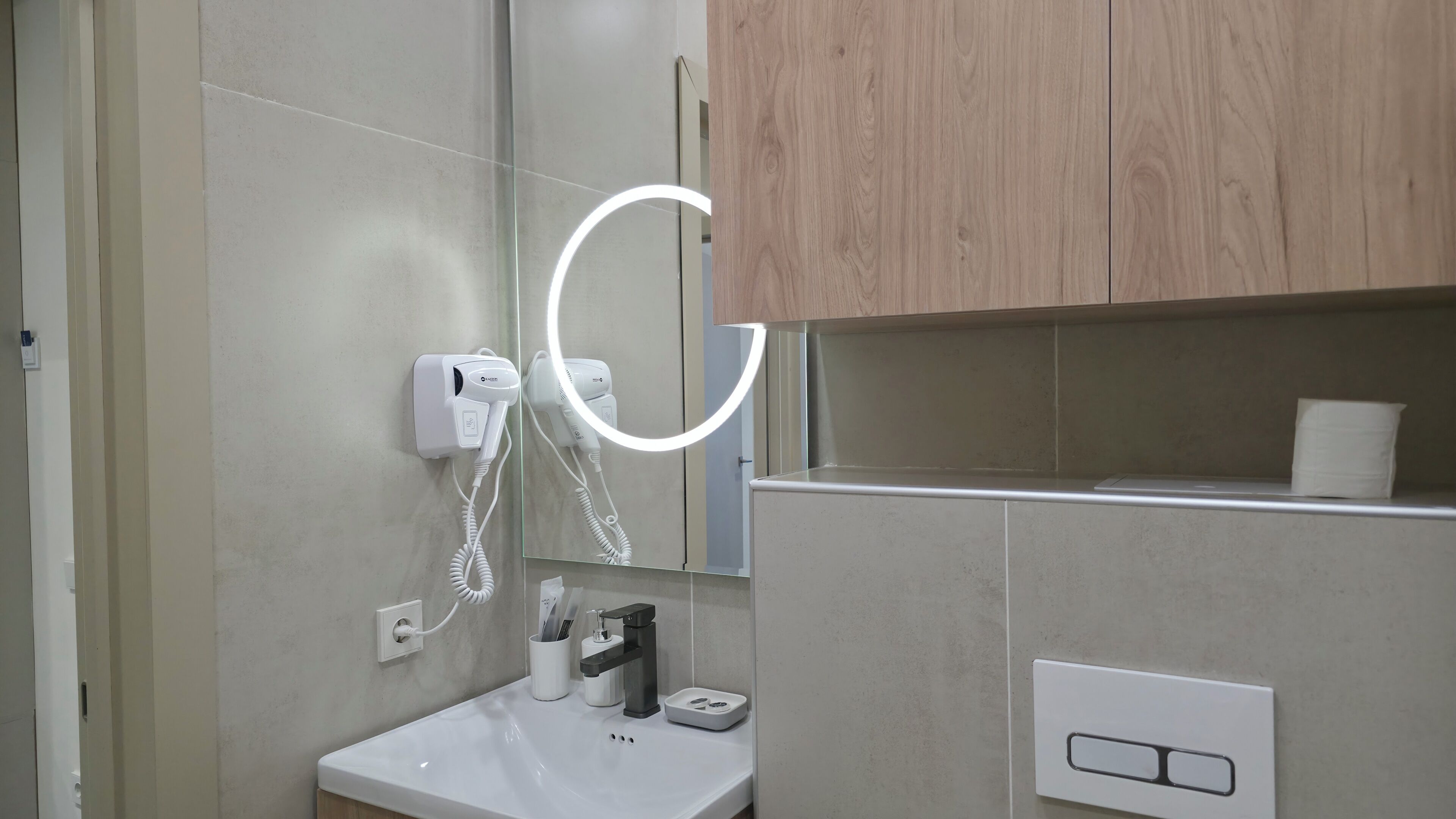 A bathroom with a mirror, a hairdryer, a sink, and a towel dispenser.
