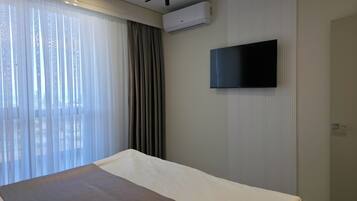 A hotel room with a bed, a television mounted on the wall, and an air conditioning unit.