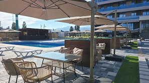 Zona de piscina al aire libre con sillones de descanso, sombrillas y un bar.