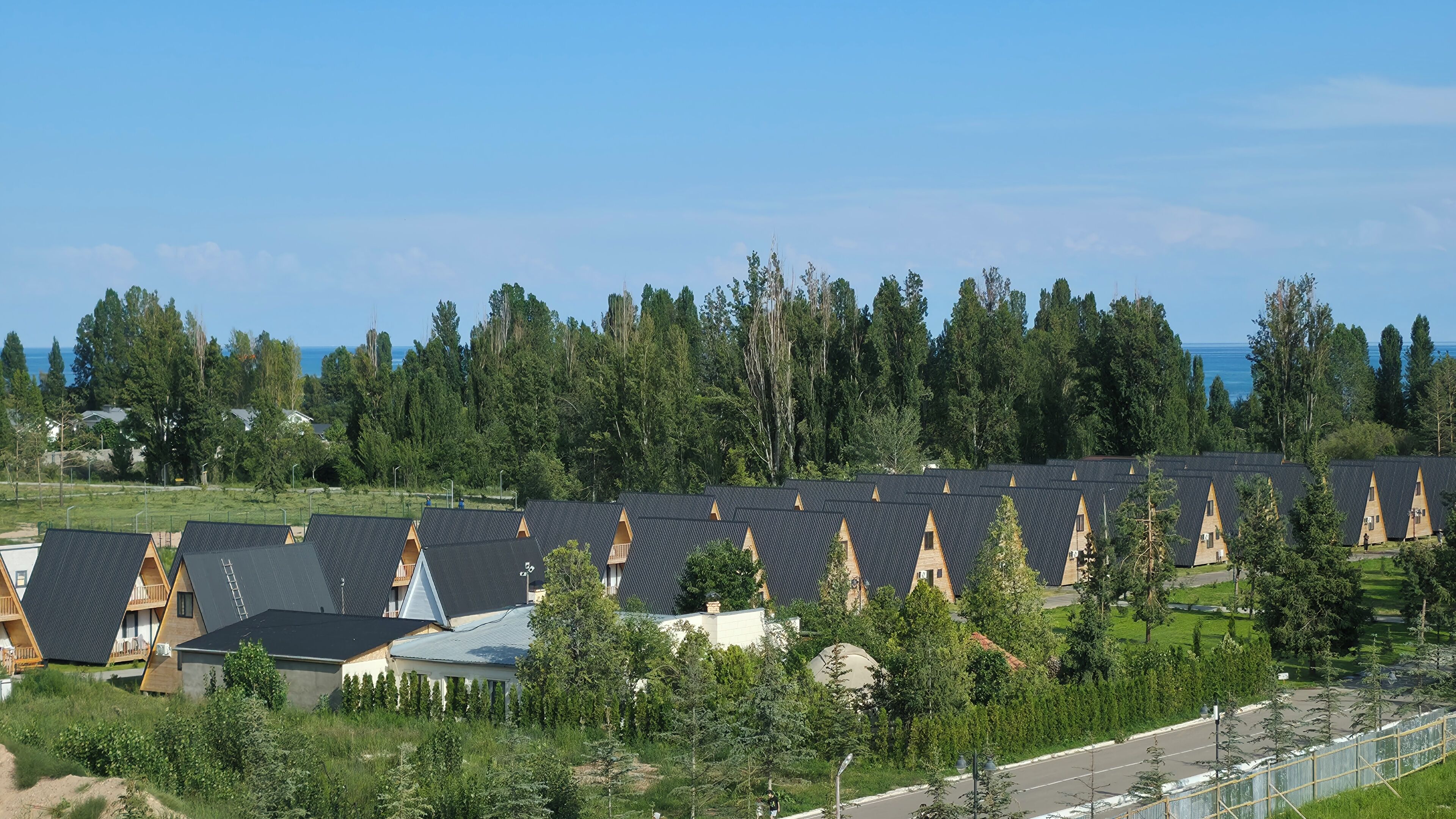 A row of A-frame cabins with a view of the sea and dense forest.