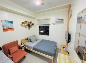 Ein Schlafzimmer mit Bett, einer Couch, einem Fernseher und einem Fenster mit Blick auf die Stadt.