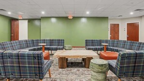 A lobby with a green wall, a central wooden table, and plaid-patterned seating.