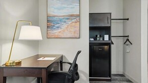 Une chambre d’hôtel équipée d’un bureau, d’une chaise, d’une lampe, d’œuvres d’art, d’un minibar et d’un porte-manteau.