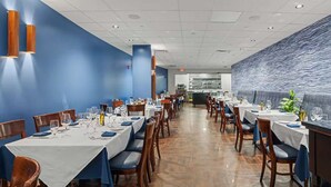 Un restaurant avec plusieurs tables et chaises, une cuisine à l’arrière-plan et un mur bleu orné d’un motif ondulé.