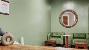 Un espace d’accueil agrémenté d’un mur végétal, d’un miroir rond, de deux fauteuils verts et d’un comptoir d’accueil en bois.