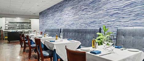 Ein Restaurant mit gedeckten Tischen, einer Küche im Hintergrund und einer strukturierten Wand.