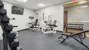 Une salle de sport équipée de divers appareils d’exercice, d’un porte-haltères et d’un panneau indiquant la sortie.