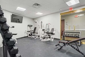 A gym with various exercise machines, a rack of dumbbells, and an exit sign.