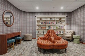 A room with a large leather ottoman, a bookshelf, a mirror, and a round table.