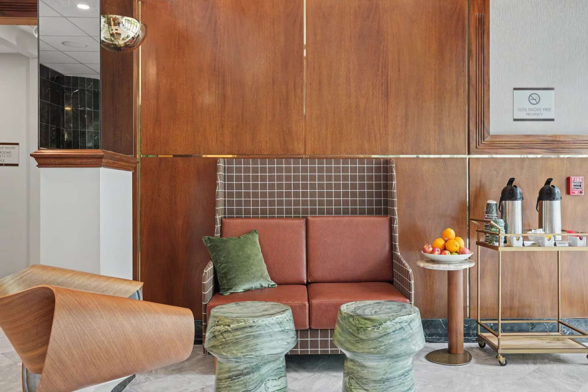 A modern hotel lobby with a seating area, a small table with fruits, and a fire extinguisher.