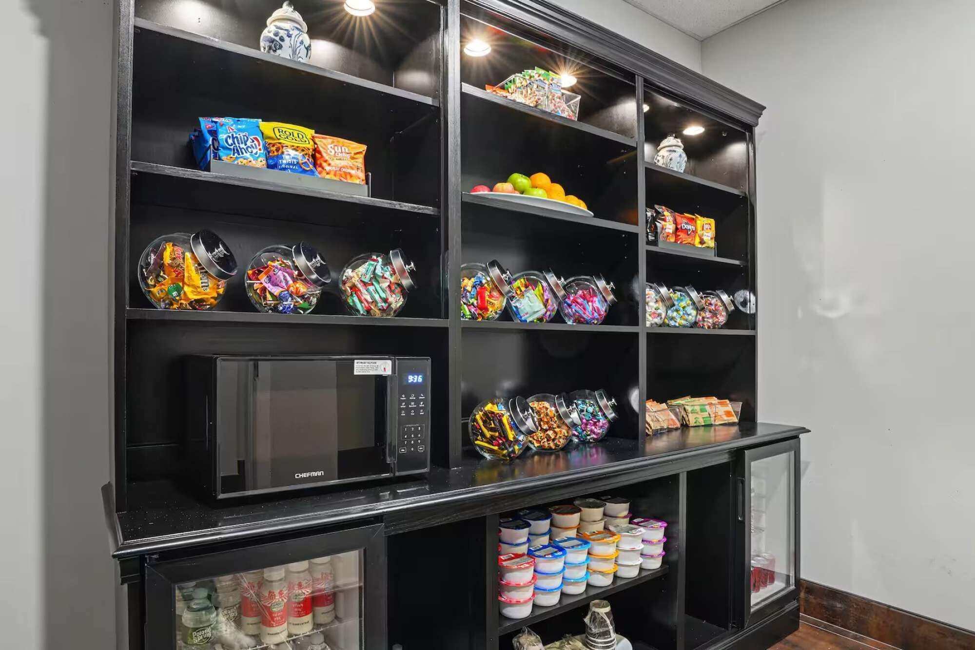 A kitchen with a built-in microwave and shelves stocked with snacks and condiments.