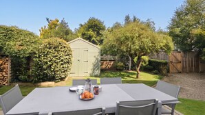 Une terrasse extérieure avec une table et des chaises, un petit abri de jardin et un jardin bien entretenu.