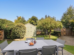 Eine Terrasse im Freien mit Tisch und Stühlen, eine kleine Gartenhütte und ein gepflegter Garten.