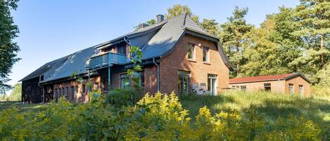 A large brick house with a balcony, surrounded by a field of yellow flowers.