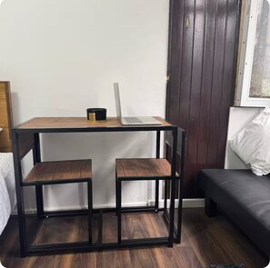 Una habitación pequeña con un escritorio de madera, dos sillas, una laptop y un sofá negro.