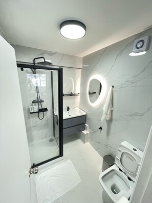 Un baño moderno con cabina de ducha de vidrio, tocador con espejo e inodoro.