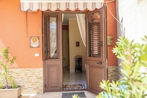 A house entrance with a wooden door, a small potted plant, and a doormat. - Casa del Sole - Menfi (Menfi)