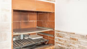 Uma cozinha com painel de parede de tijolos, uma prateleira de metal e bancada branca.