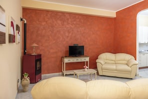 Ein Wohnzimmer mit einer Couch, einem Fernseher auf einem Schrank, einem kleinen Tisch und einem Schrank.