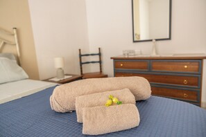Un lit bien fait, recouvert d’une couvre-lit bleue, une table de chevet en bois avec une lampe et une commode avec un miroir.