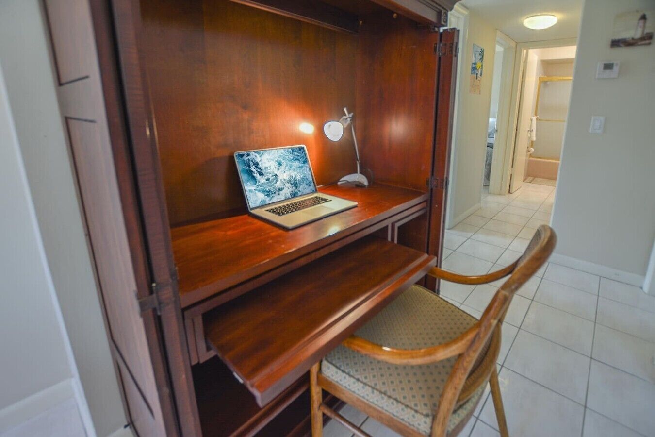 Un bureau en bois avec un ordinateur portable et une lampe de bureau, une chaise et un sol carrelé.