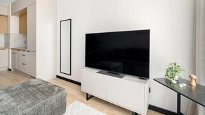 Ein modernes Wohnzimmer mit Flachbildfernseher, einer Couch, einer Essecke mit Schränken und einem kleinen Tisch mit Pflanze.