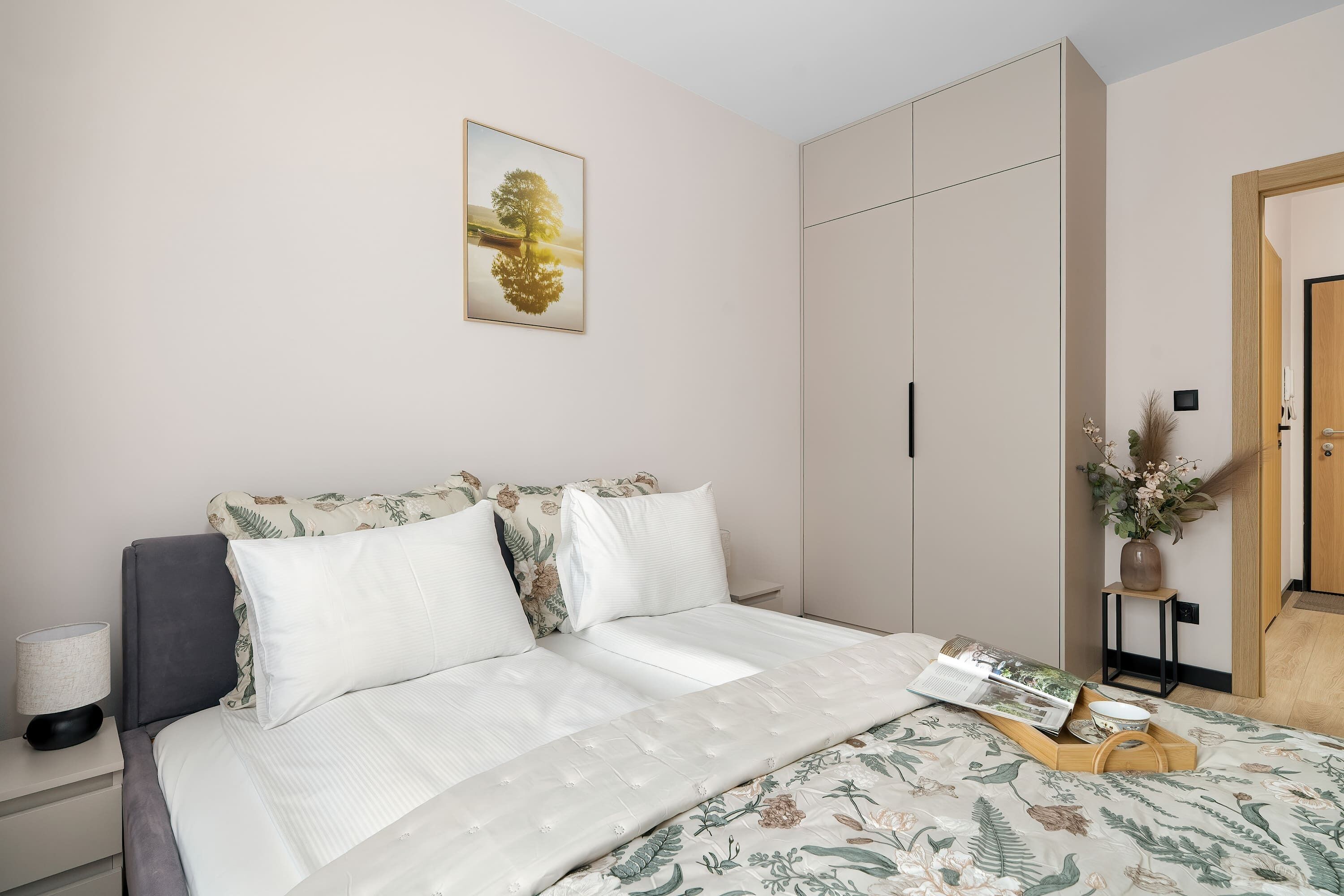 A bedroom with a bed, a nightstand, a bedside table, a wardrobe, and a door.