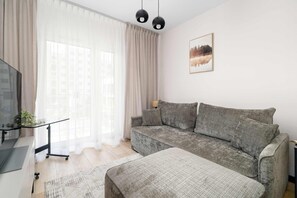 Un salon moderne avec un canapé gris, une petite table d’appoint et un téléviseur.