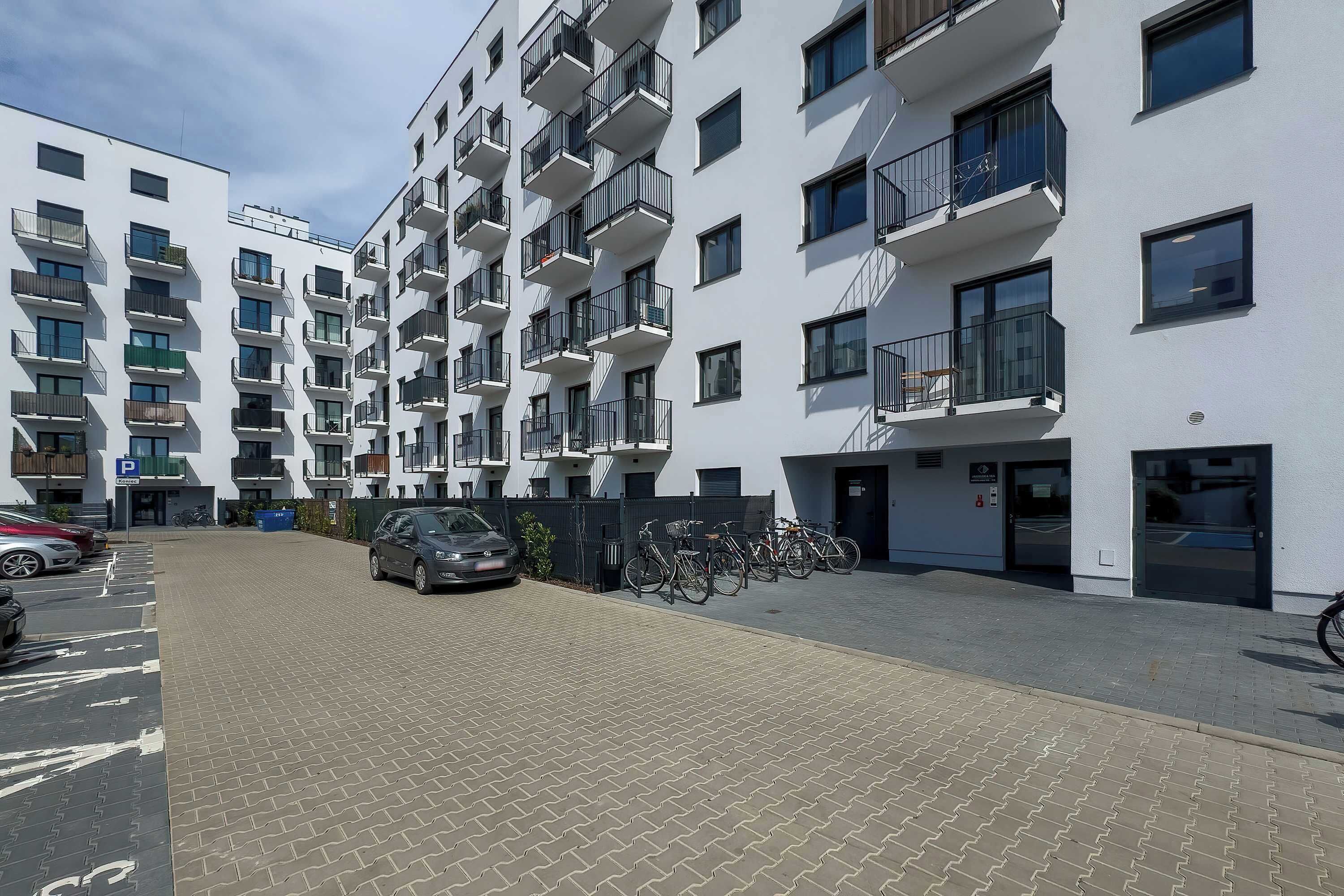 A multi-story residential building with balconies, a parking area, and a bicycle parking area.