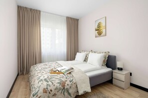 Un dormitorio con cama, mesita de noche, lámpara, un cuadro enmarcado en la pared y una ventana con cortinas.