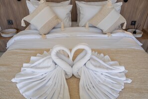 A hotel room with a neatly made bed, two pillows, and a towel arrangement in the shape of swans. - Villa Temple of Tides (badung)