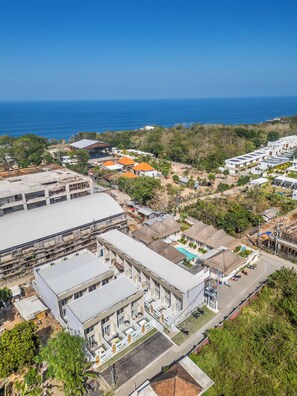 A coastal resort with multiple buildings, including a large hotel with a swimming pool and a smaller building with a thatched roof. - Villa Temple of Tides (badung)