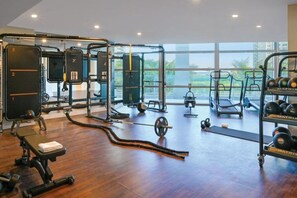 Ein Fitnessraum mit unterschiedlichen Trainingsgeräten, großen Fenstern und Holzboden.