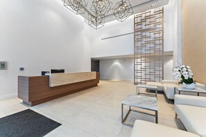 A modern reception area with a wooden reception desk, seating arrangements, and a decorative wall panel. - 2BR 2BA in a New Amrit Beach Resort Peace Tower (Riviera Beach)