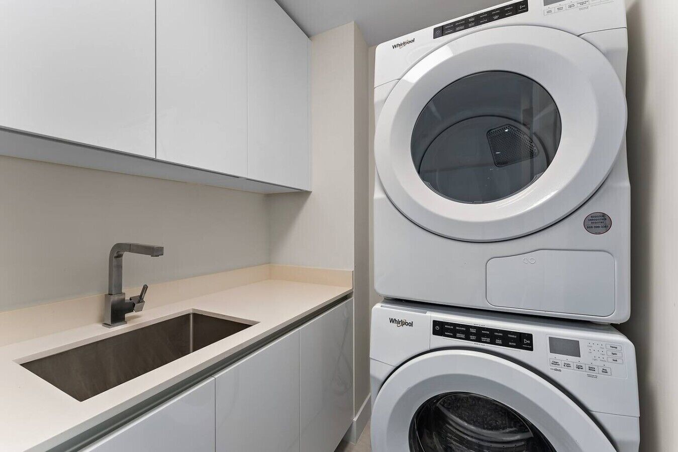 A modern laundry room with a stacked washer and dryer, a sink, and a cabinet.
