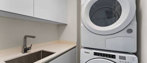 A modern laundry room with a stacked washer and dryer, a sink, and a cabinet.