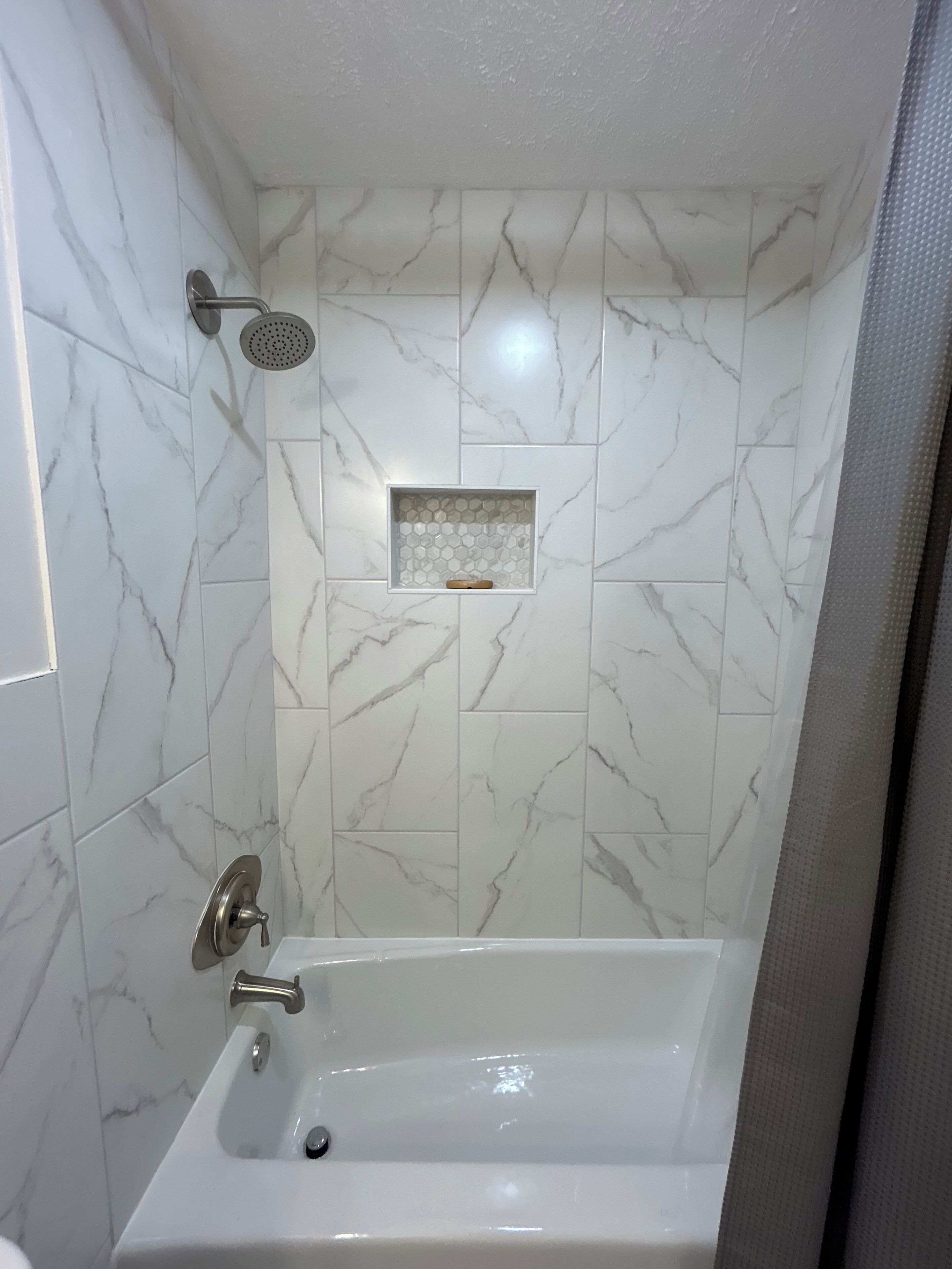 A bathroom with a bathtub, a shower, and a tiled wall with a marble pattern.