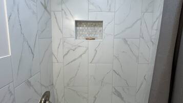 A bathroom with a bathtub, a shower, and a tiled wall with a marble pattern.