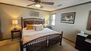 A bedroom with a wooden bed, two bedside tables with lamps, a ceiling fan, a framed picture on the wall, and a window with blinds. - Welcome to the Bay House! (St George Island)