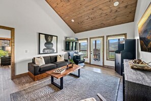 A spacious living room with a wooden ceiling, a sofa, a coffee table, and a television. - Stunning Mountain Views! 3BR Cabin w/ Hot Tub, Fire Pit & Games (Gatlinburg)