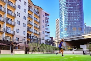 A tennis court with two players in action, surrounded by modern apartment buildings. - Kivuli | Walk to Elizabeth Quay • Pool • Parking (Perth)