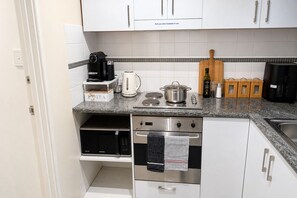 A modern kitchen with white cabinets, a built-in microwave, a stainless steel oven, and a coffee maker on the counter. - Kivuli | Elegant 1BR • Perth CBD • Parking. (Perth)