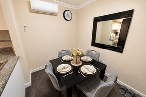 A dining area with a table set for four, a clock, and a mirror on the wall. - Kivuli | Elegant 1BR • Perth CBD • Parking. (Perth)